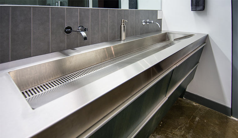 Custom fabricated stainless steel sink with two wall mounted faucets and one linear drain in downtown Des Moines loft remodel by Silent Rivers