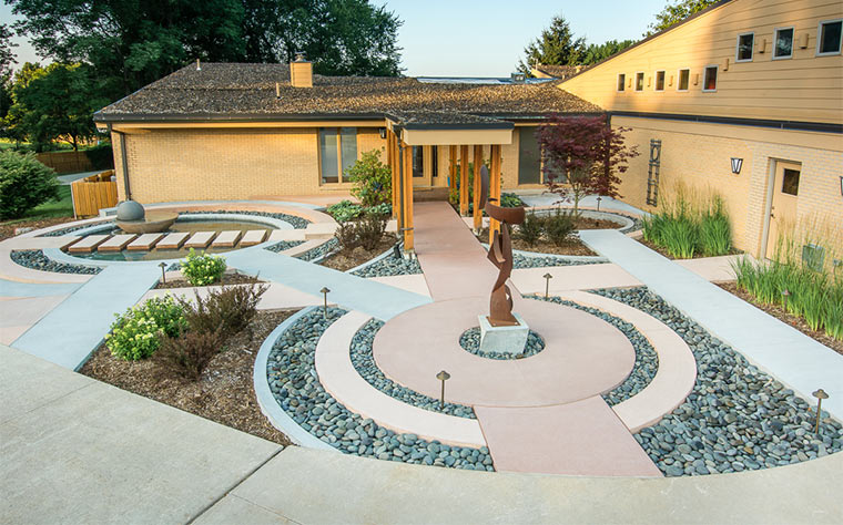 A series of rings intersect for pathways in this front courtyard with sculpture and water feature in Johnston, Iowa by Silent Rivers