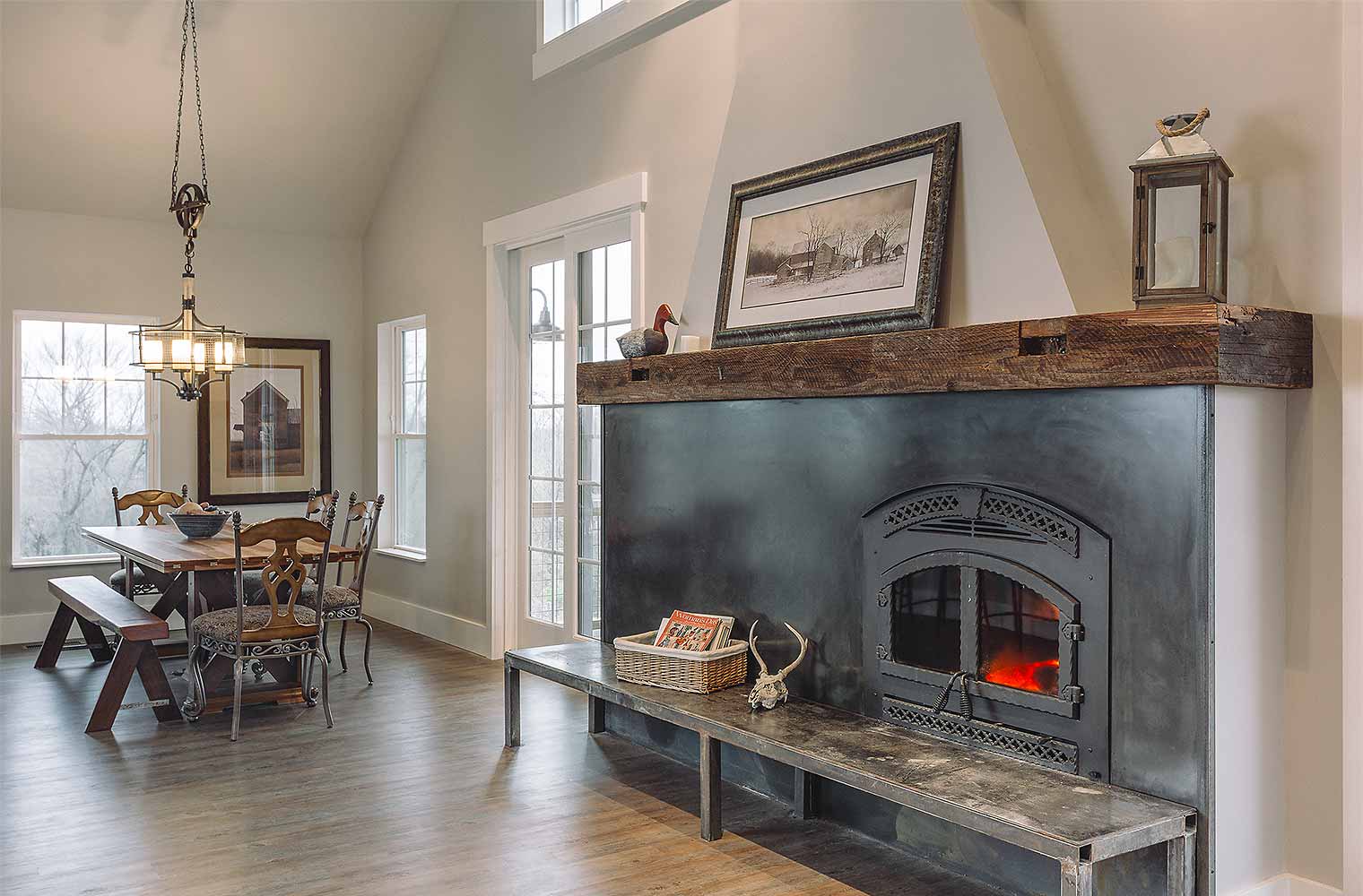 Steel hearth fireplace with reclaimed barn wood mantel anchors the living room and dining room of barn style custom new home in St. Charles, Iowa designed and built by Silent Rivers of Des Moines