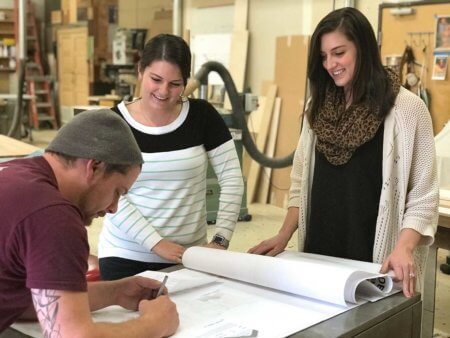 Caitlin Cuevas and Aime Conrad review architectural plans with woodshop artisan Alex Schlepphorst.