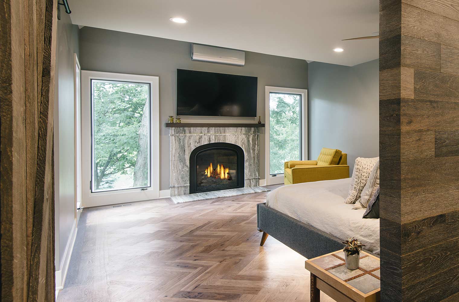 contemporary master suite features three way mirror, gas fireplace, marble mantel, tall casement windows, herringbone oiled floor by designer and remodeler Silent Rivers of Des Moines, Iowa