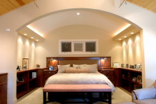 Cove lights, warm wood built-ins, and a gently arched ceiling create a master bedroom retreat