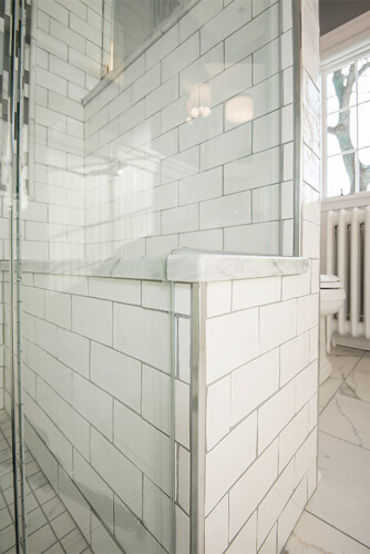 Des Moines, Iowa craftsman bathroom remodel by Silent Rivers features a tiled shower with marble bench that extends through glass surround