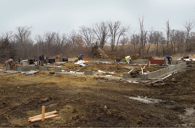 Construction has begun on new home by Silent Rivers in Iowa, concrete forms are being removed from foundation stub walls.