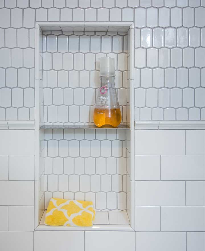 Stainless steel shower shelf in white tile shower with subway tile and hexagon tile by bathroom remodeler Silent Rivers, Des Moines