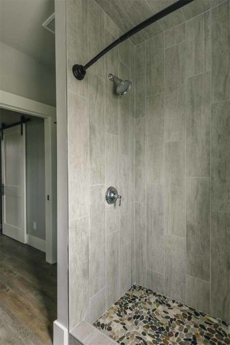 Industrial farmhouse style custom new home in St. Charles, Iowa designed and built by Silent Rivers of Des Moines features a shower with large vertical tile, curved shower bar and stone-like floor tile.