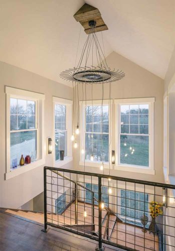 industrial farmhouse style custom new home in St. Charles, Iowa designed and built by Silent Rivers features a grand staircase made of steel channel and bridge plank lumber and hay wheel chandelier custom light fixture