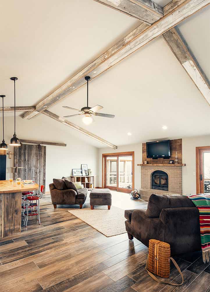 Rustic family room with upcycled barn wood ceiling beams, fireplace, patio doors designed and built by Silent Rivers in central Iowa for a rural Iowa retreat
