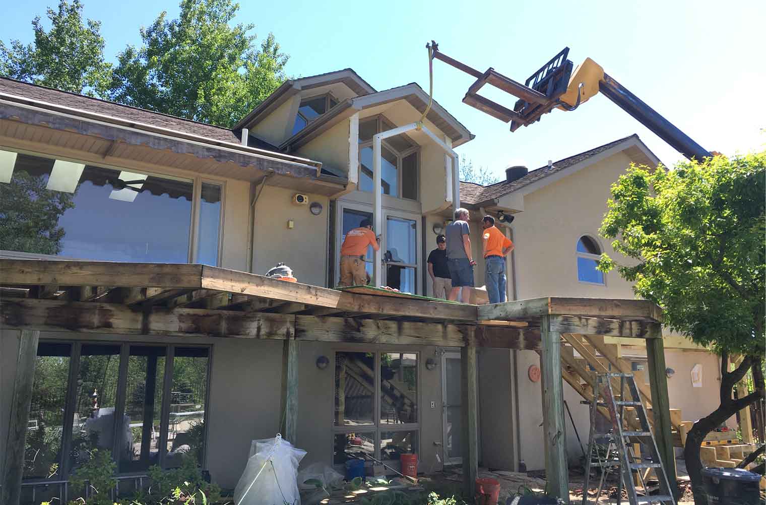The first piece of metal armature for the new arbor on this rural Iowa deck designed and built by Silent Rivers of Des Moines is hoisted up with heavy equipment