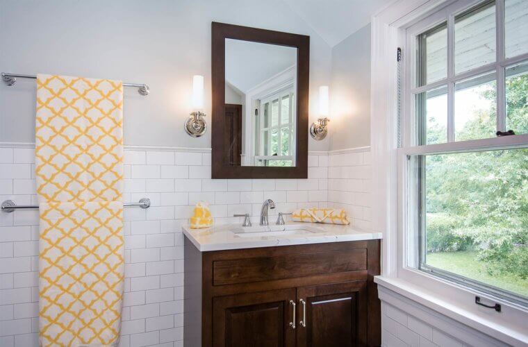 custom vanity cabinet in dark stain, white marble vanity top, chrome faucet, wall sconces, matching mirror, white tile wainscot in Des Moines bathroom by remodeler Silent Rivers