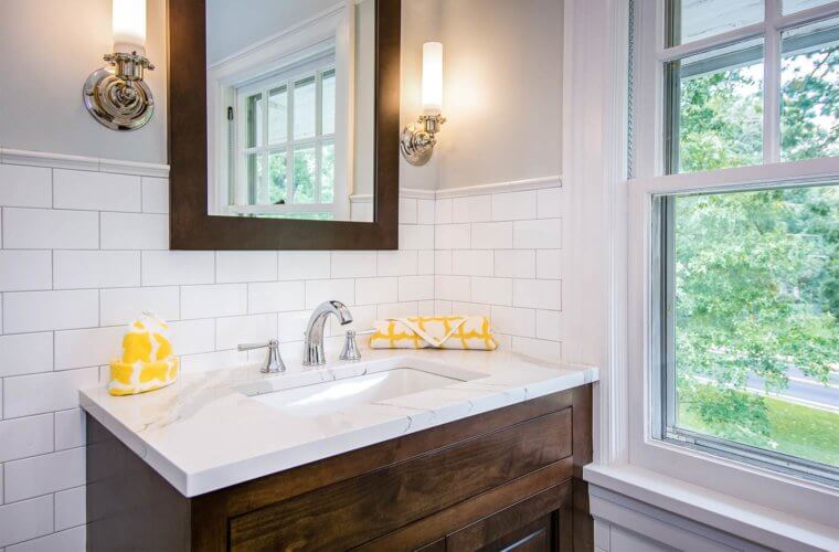 custom vanity cabinet in dark stain, white marble vanity top, chrome faucet, wall sconces, matching mirror, white tile wainscot in Des Moines bathroom by remodeler Silent Rivers