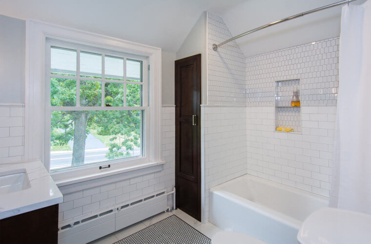 penny round floor tile with white marble border, cast iron tub with white tile shower surround and custom storage tower in Des Moines bathroom by remodeler Silent Rivers