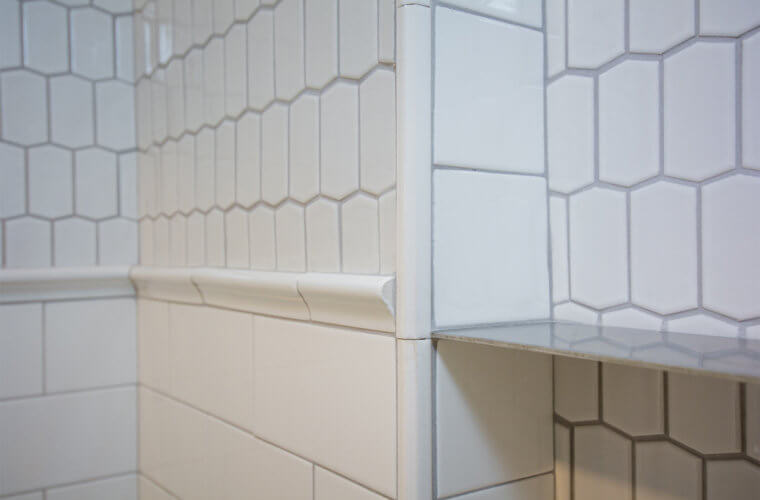 white elongated hexagonal tile above the white subway tile wainscot shower with inset shelf in Des Moines bathroom by remodeler Silent Rivers