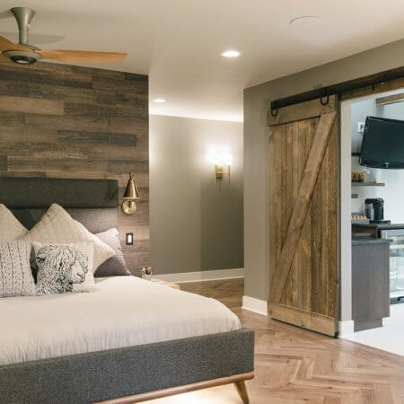 view from master bedroom into bathroom shows wood wall, sliding barn door, herringbone floor in master suite remodel by Silent Rivers of Des Moines