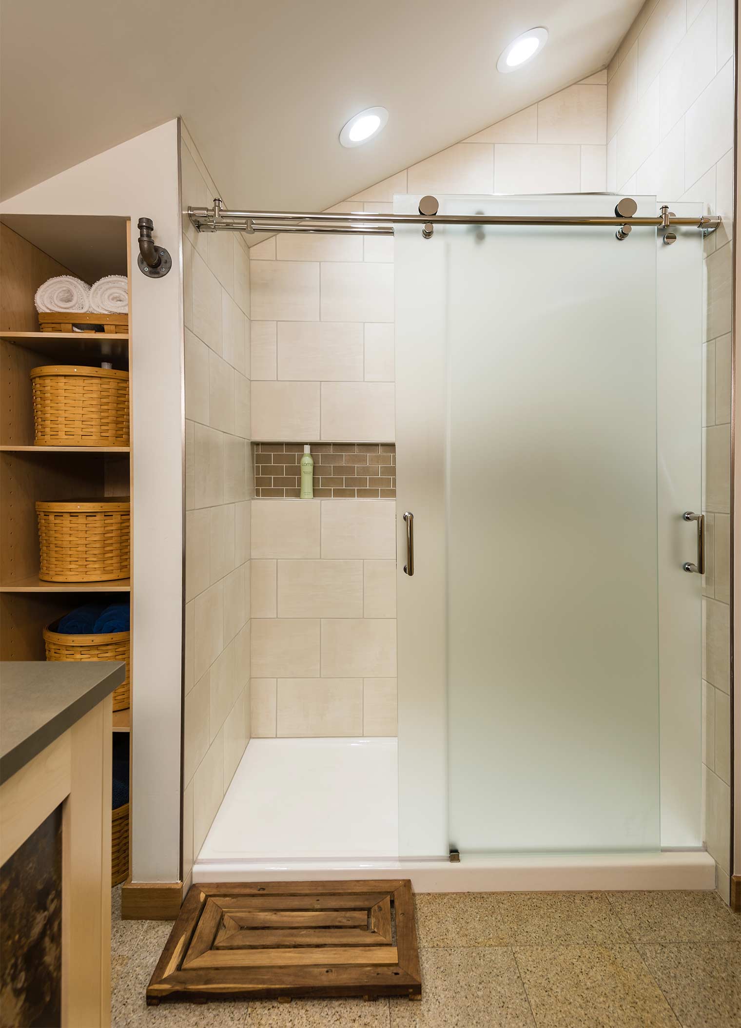 frosted glass sliding shower doors hang from chrome rolling bar in ceramic tiled shower with open shelving unit in Johnston bathroom by remodeler Silent Rivers