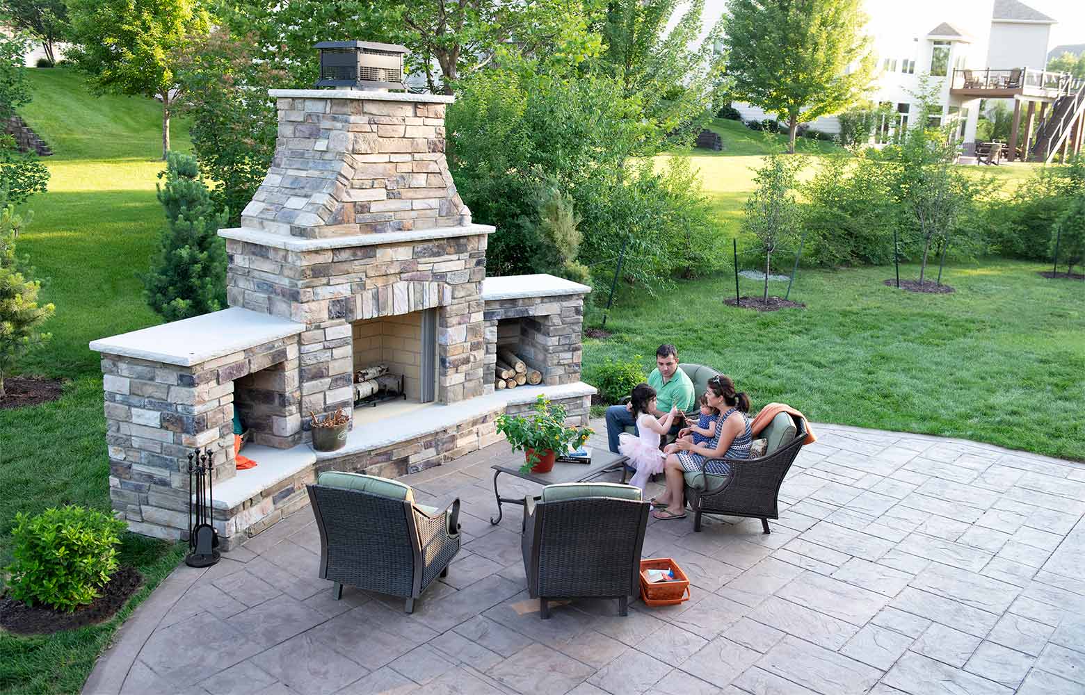 Family of four relaxing by their outdoor fireplace by Silent Rivers at their Urbandale IA home