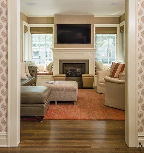 An addition on a historic colonial farmhouse contains a sunroom with walls of windows, cozy fireplace and built-in benches.