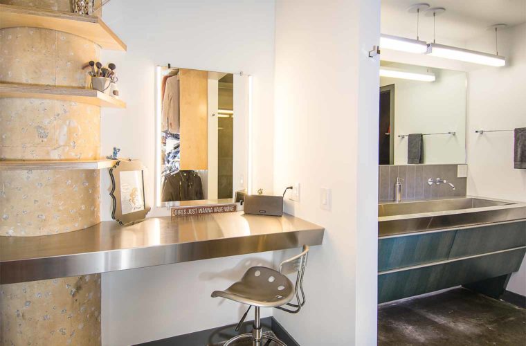 Close and make-up area with birch shelves built around concrete column next to stainless steel trough sink in downtown Des Moines loft remodel by Silent Rivers
