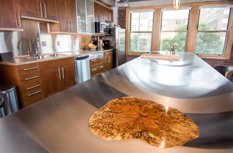 A polished silver maple tree section integrated into stainless steel kitchen island in downtown Des Moines loft remodeled by Silent Rivers