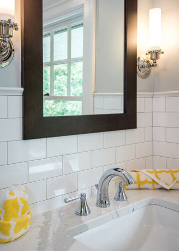 white subway tile wainscot, white marble counter, chrome faucet, custom vanity cabinet with matching mirror, sconces in Des Moines bathroom by remodeler Silent Rivers