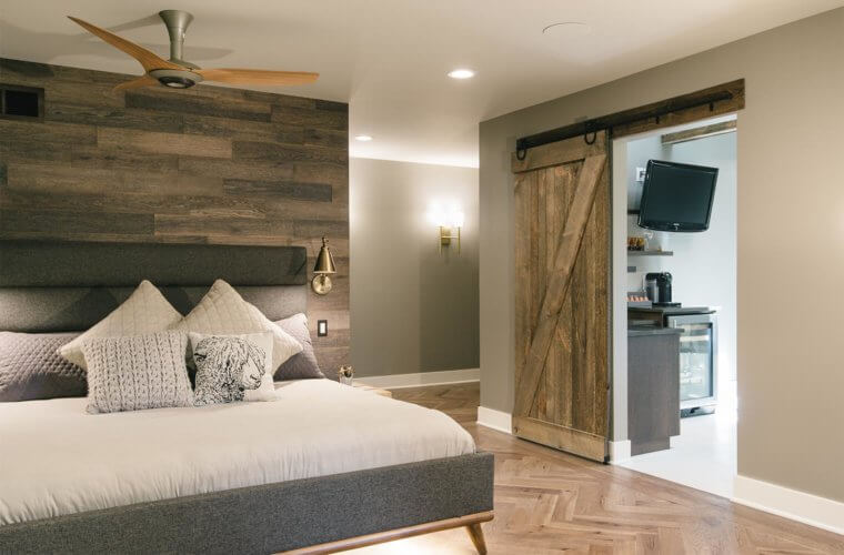 view from master bedroom into bathroom shows wood wall, sliding barn door, herringbone floor in master suite remodel by Silent Rivers of Des Moines